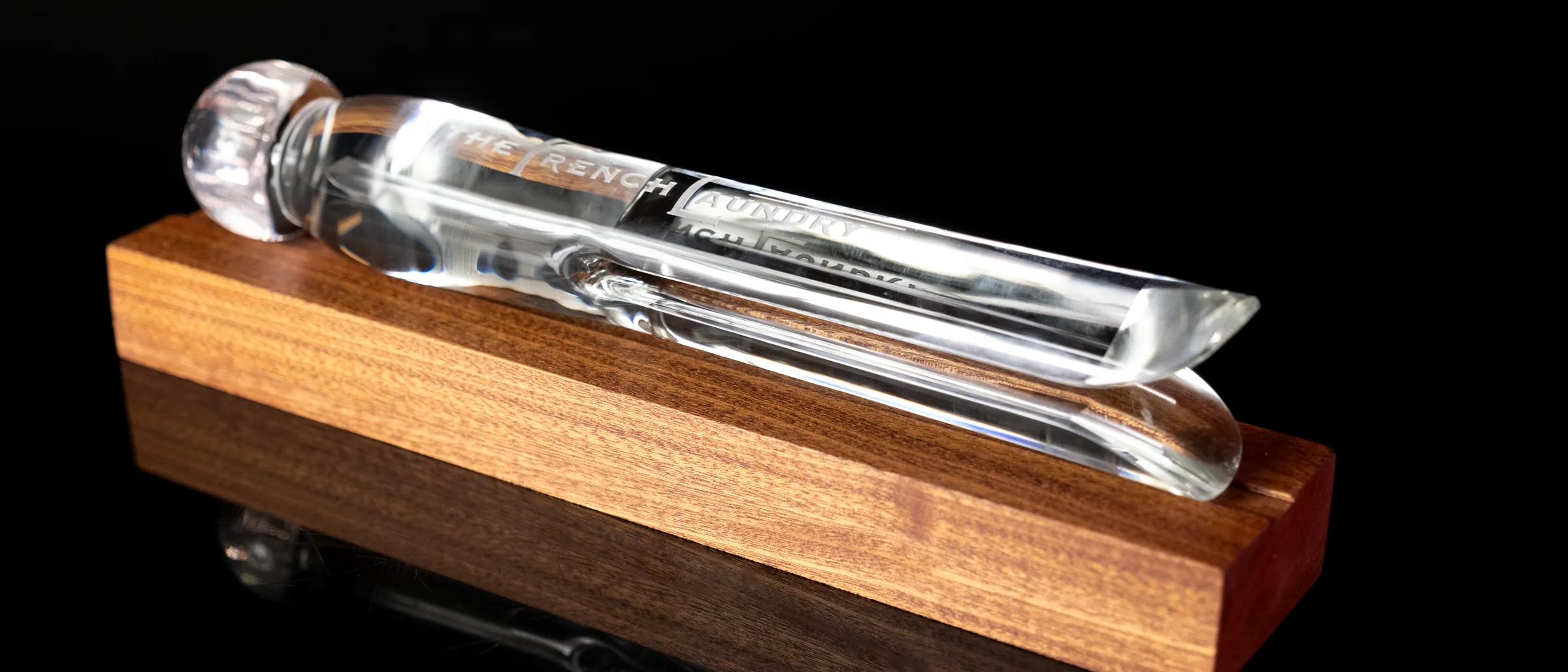 The French Laundry glass pin on its walnut base, seen from the side against black