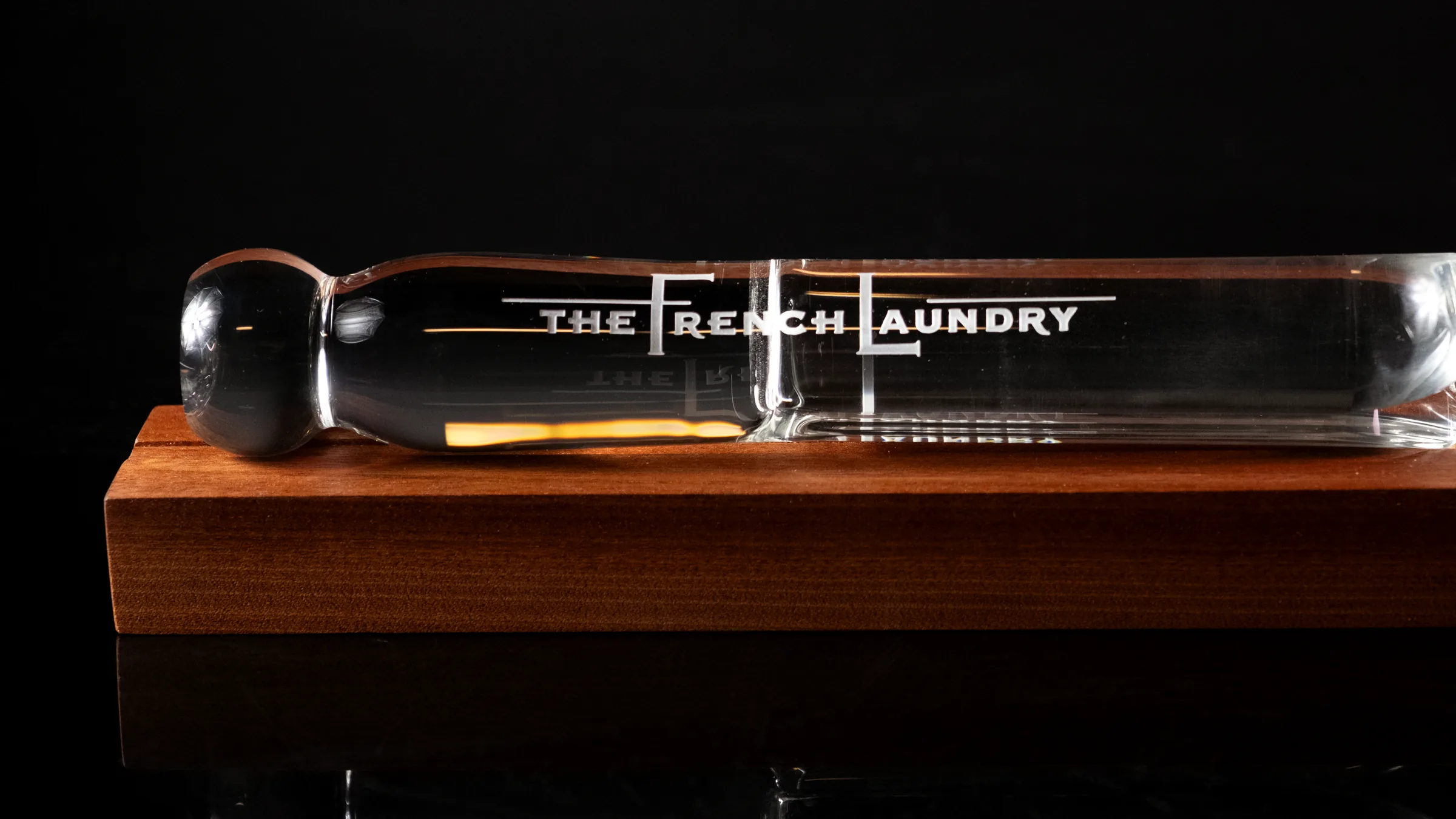 A clear hand-sculpted glass pin engraved The French Laundry, resting on a walnut base against black