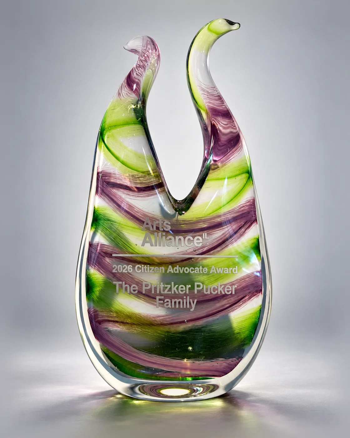 Violet and green sculpted glass award with two curving necks, lettered Arts Alliance Illinois 2026 Citizen Advocate Award, The Pritzker Pucker Family