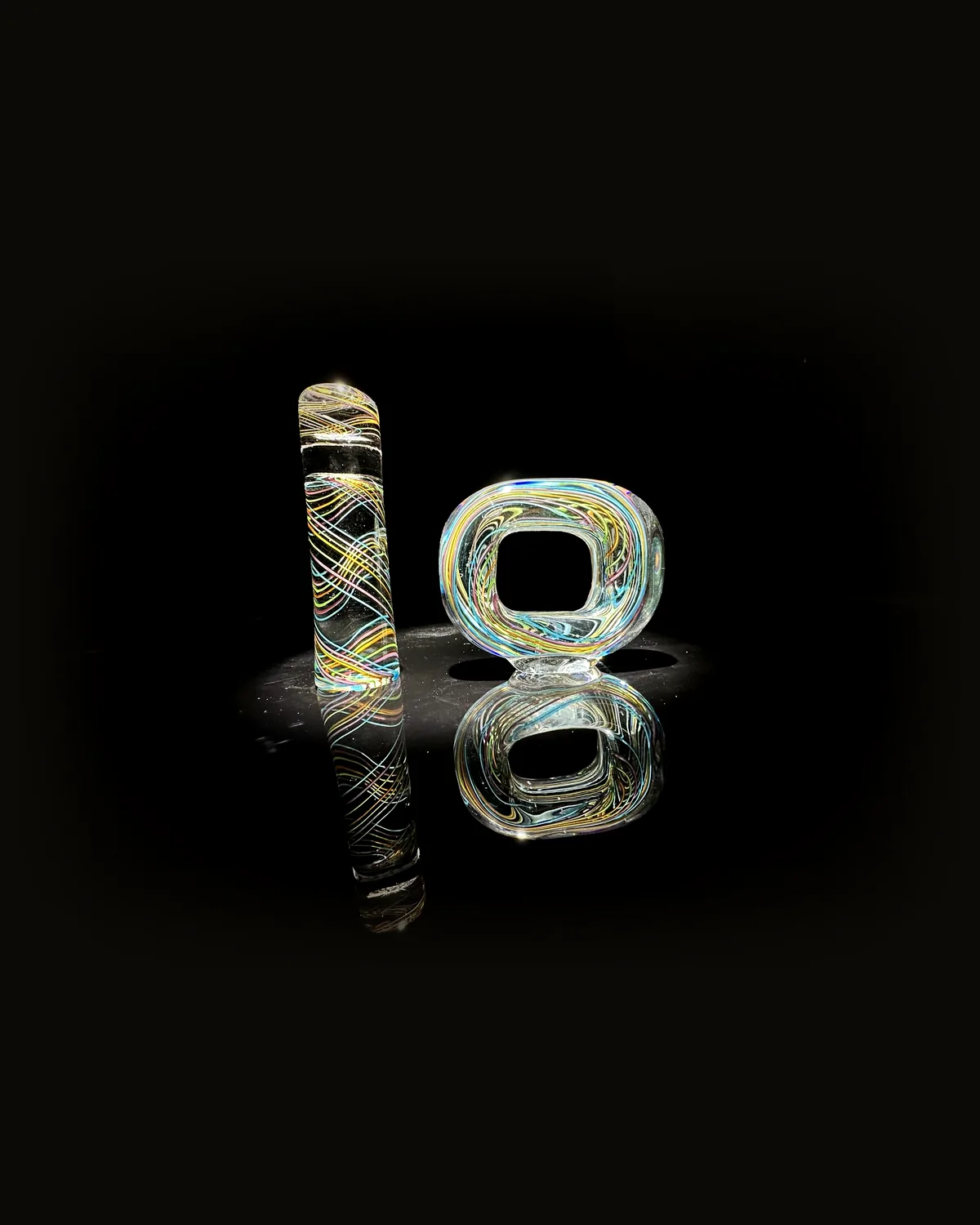 A glass column and a glass ring in multicolored cane work, the letters I and O, on a black mirror
