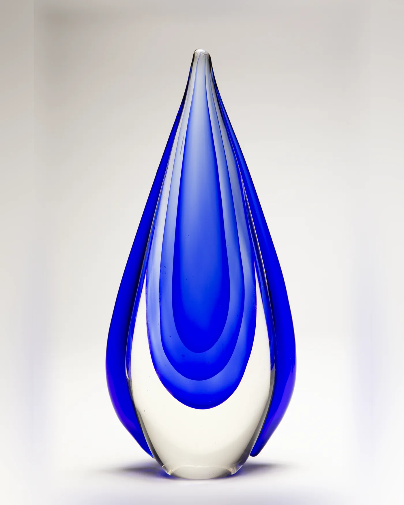 Solid cobalt blue glass teardrop award with clear outer layers on a white backdrop