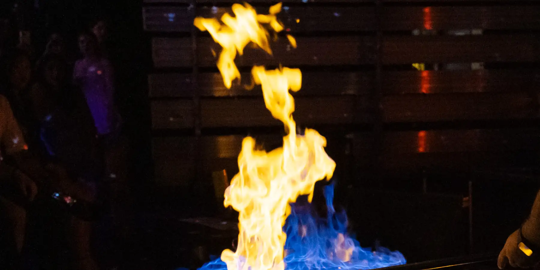 Flame and blue fire rising from the bench during a live glassblowing demonstration in the hot shop
