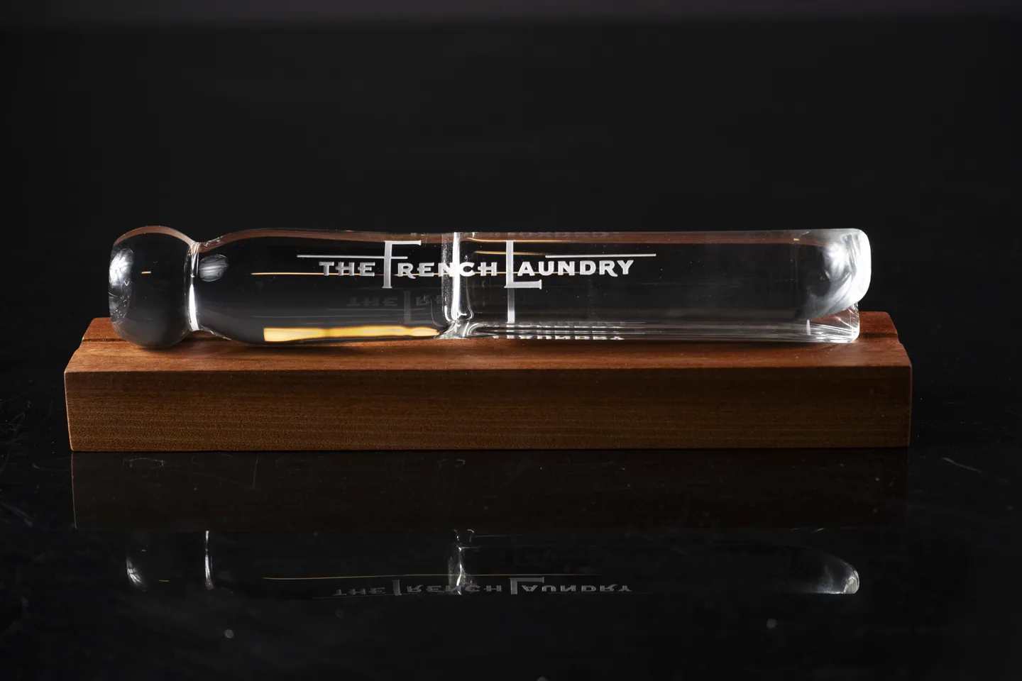 Front view of a clear glass pin-shaped piece on a wooden base.