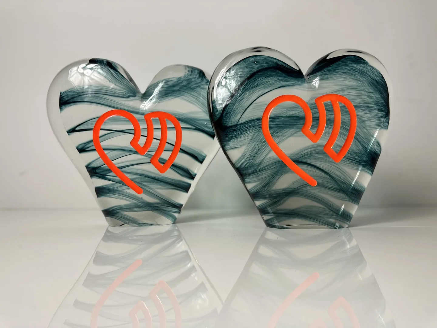 Two smoky teal glass hearts with flowing internal patterns and orange emblems.